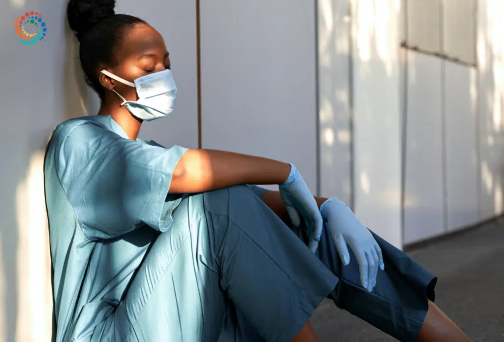 Burned out doctor sitting on the floor with eyes closed leaning against the wall